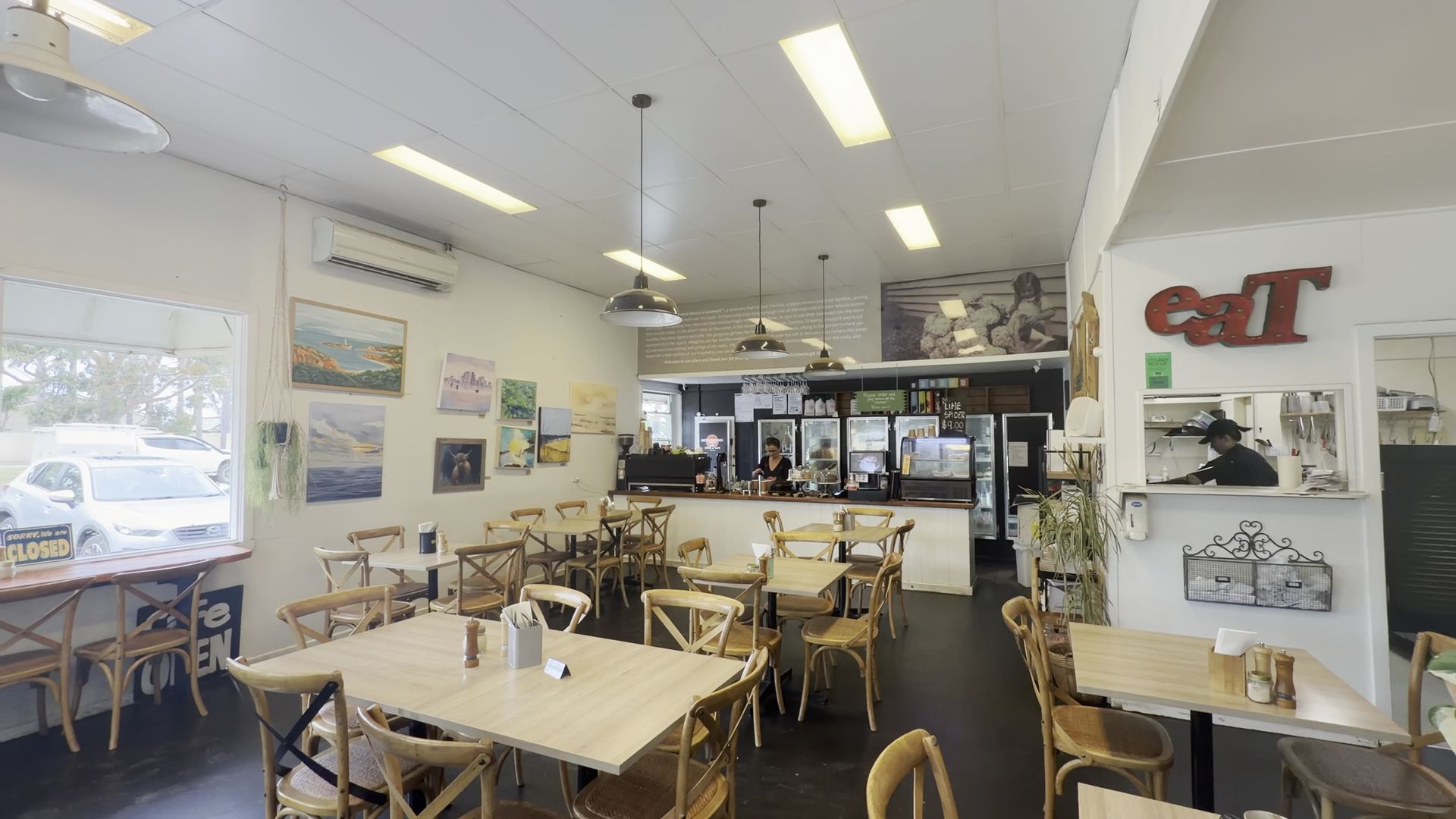 Hicksborough cafe dining room with pine chairs, local artwork on walls, and cafe counter in background