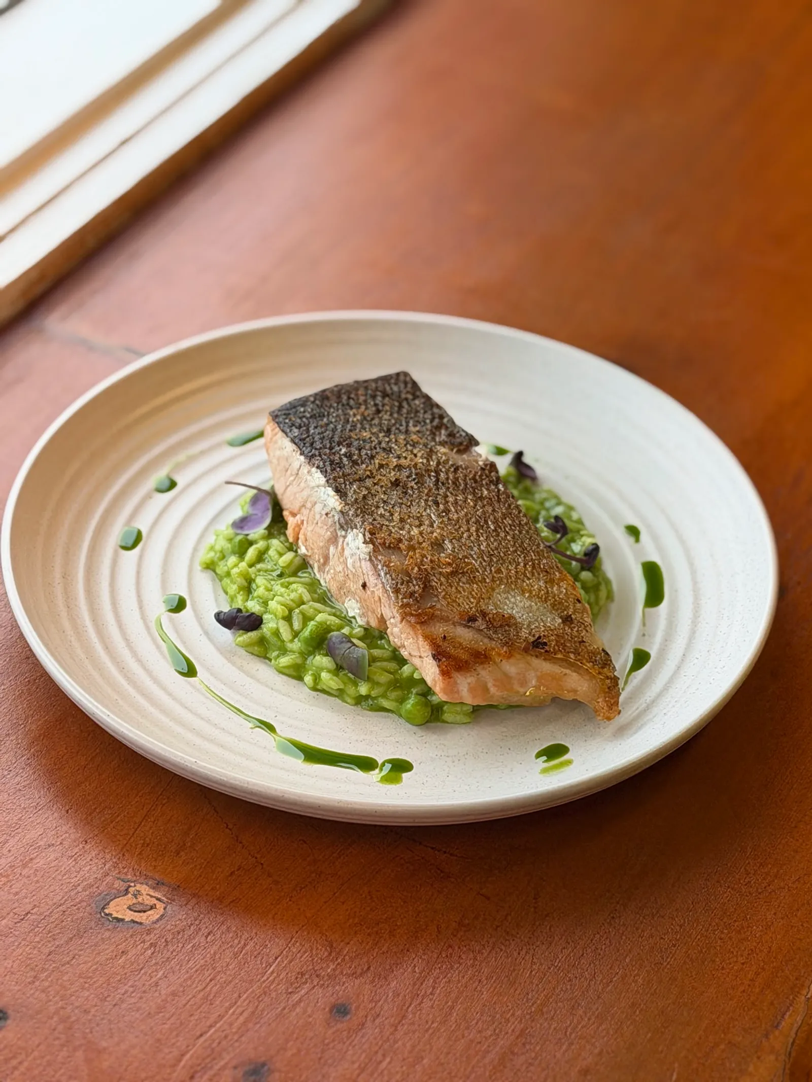 Pan-seared fish fillet with crispy skin on green pea risotto, served on a textured ceramic plate
