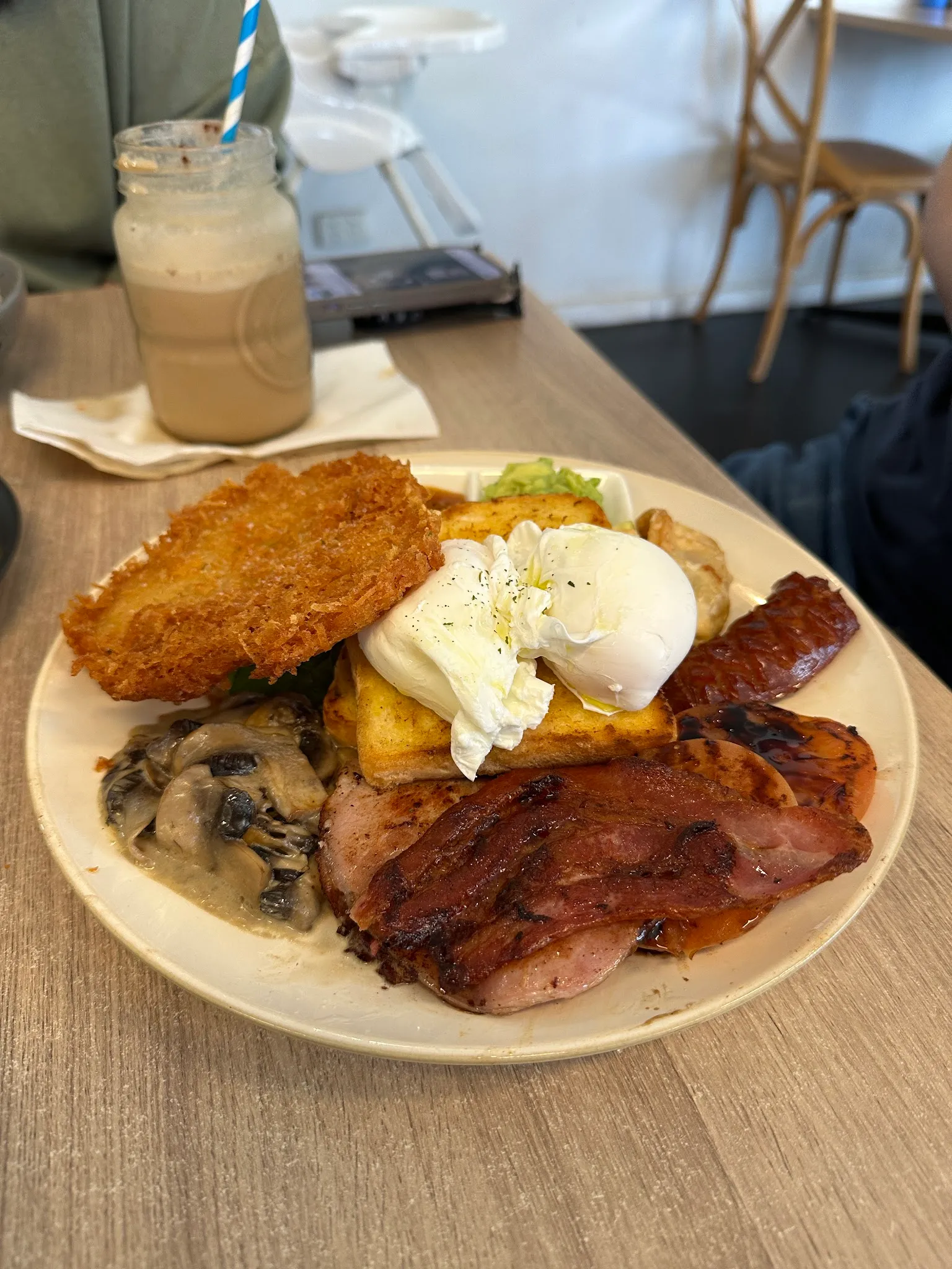 Full cooked breakfast with hash brown, poached egg, mushrooms and bacon on a white plate
