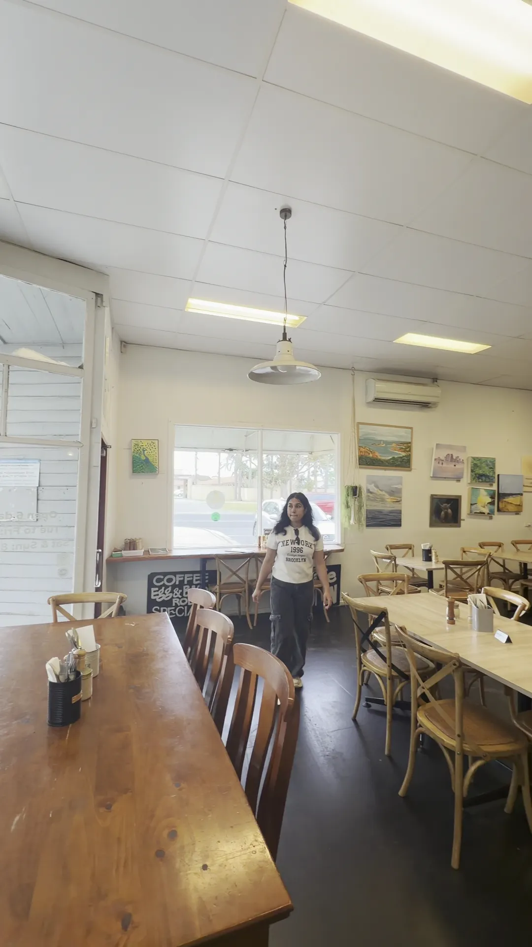 Hicksborough cafe interior with communal timber tables, cross-back chairs and local artwork on white walls