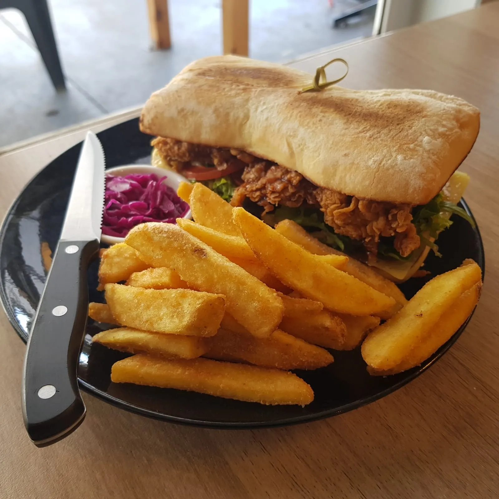 Chicken schnitzel ciabatta roll with chips and coleslaw on a black plate