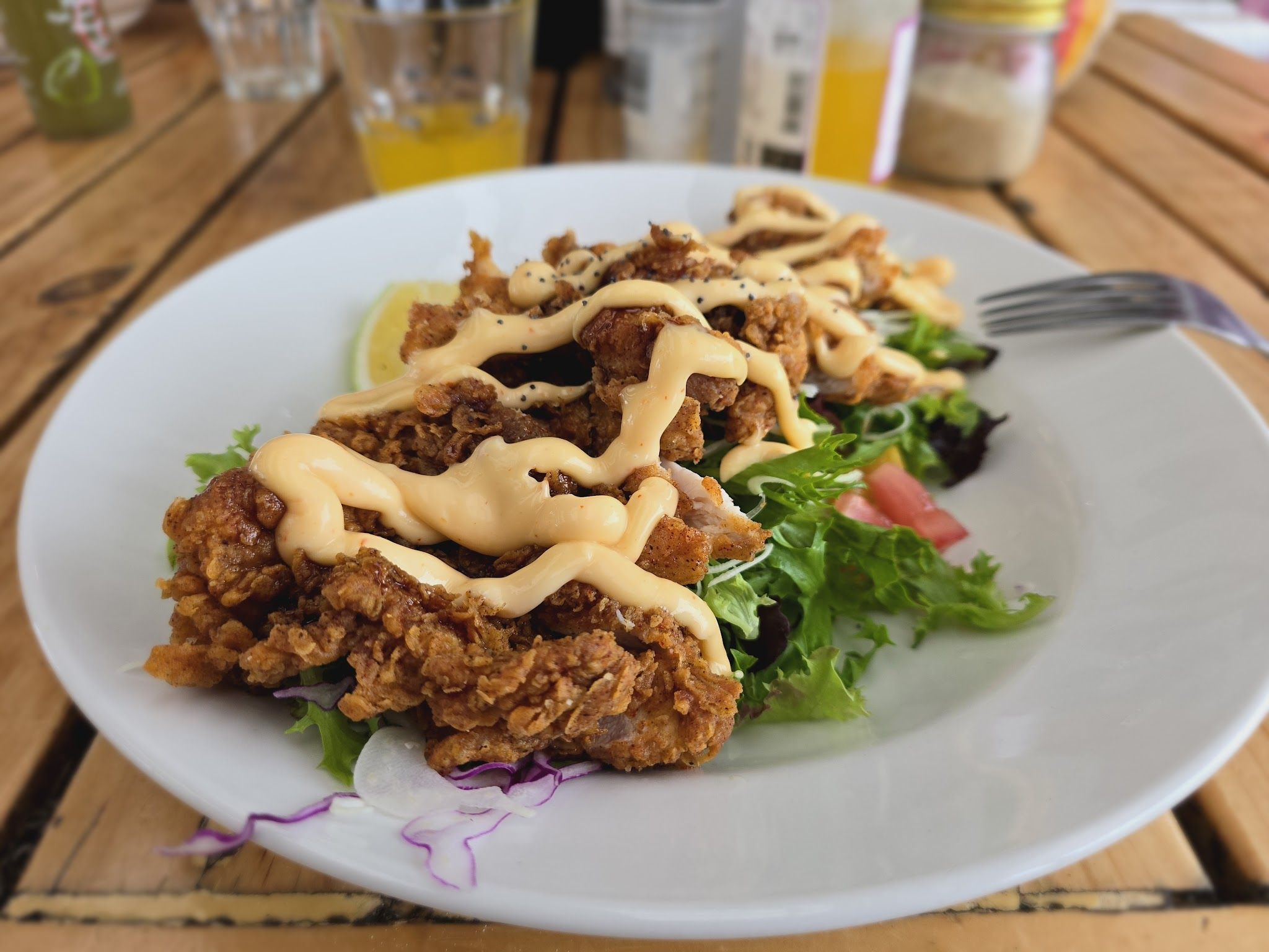 Crispy fried chicken salad on a white plate at an outdoor timber table