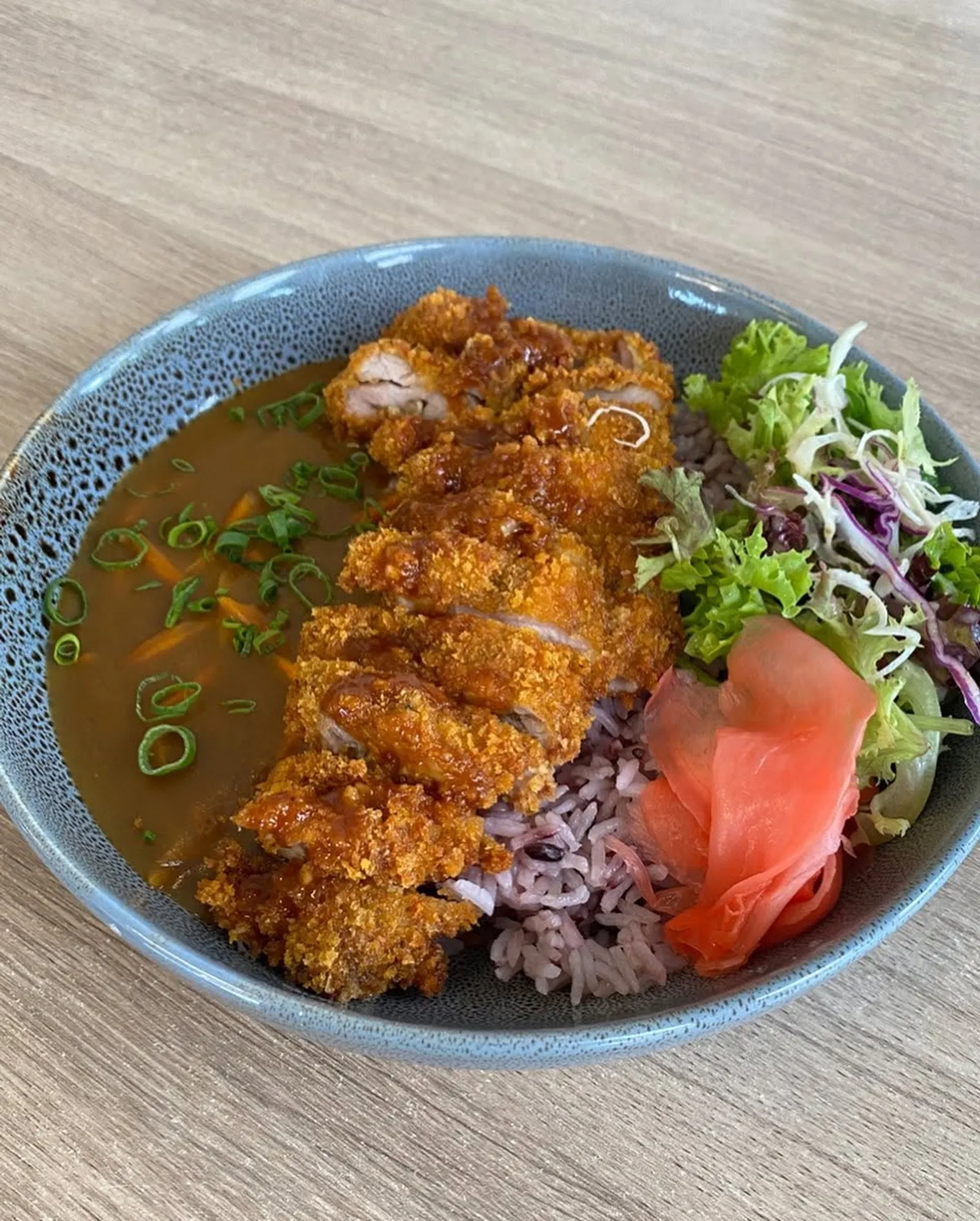 Japanese chicken katsu curry bowl with rice, slaw and pickled ginger in a grey ceramic bowl